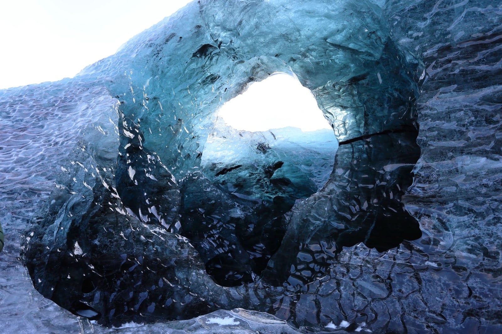 Textured blue glacial ice surrounds a circular opening inside an ice cave at Vatnajökull Glacier.