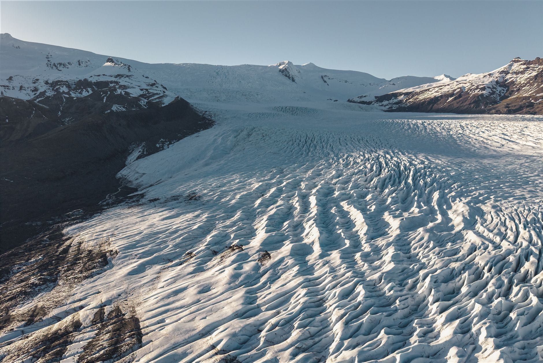 High-angle view across the vast, heavily crevassed ice field of Vatnajökull Glacier framed by snow-covered mountains.