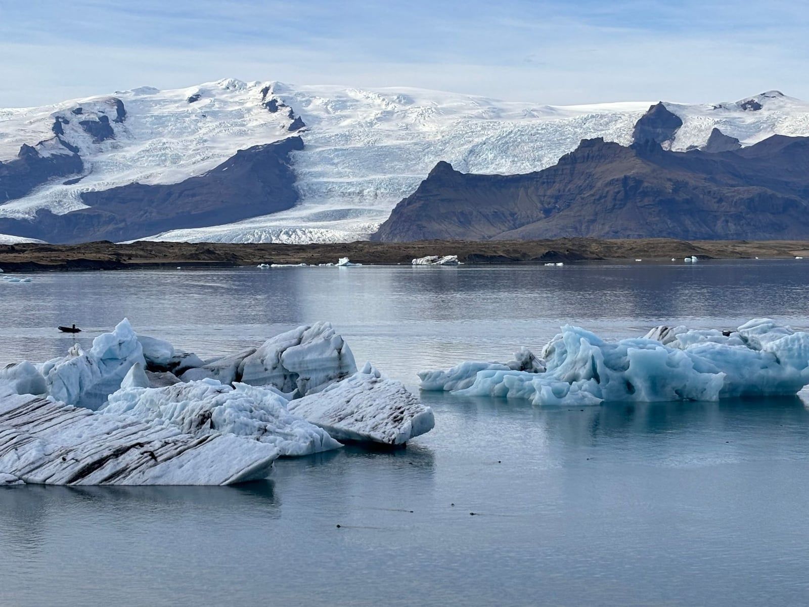 Icebergs float in Jökulsárlón glacier lagoon beneath the snow-covered tongue of Vatnajökull Glacier.