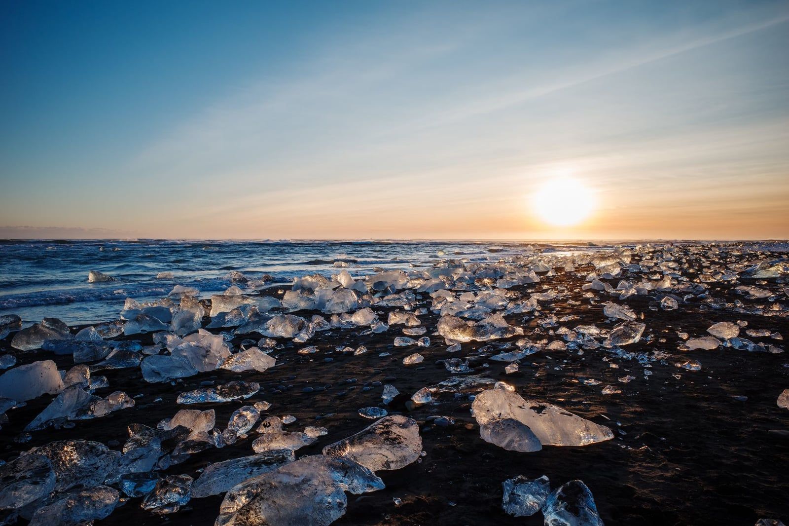 Blocks of ice from Vatnajökull Glacier glisten in the sunlight across the black sand shore at Diamond Beach.